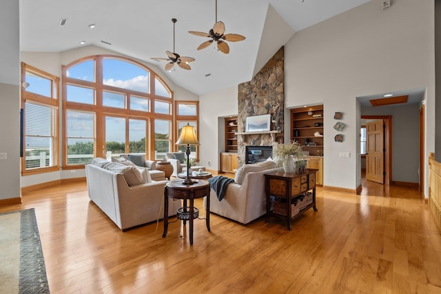 living area with high vaulted ceiling, a stone fireplace, light wood-style flooring, and baseboards