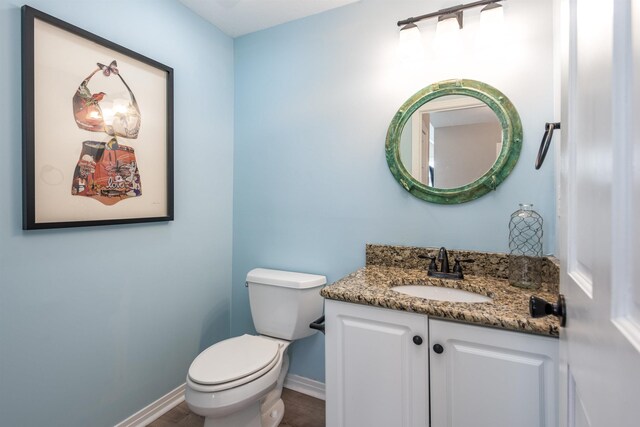 half bath featuring baseboards, toilet, wood finished floors, and vanity