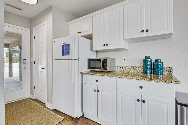 kitchen featuring visible vents, stone countertops, freestanding refrigerator, white cabinets, and stainless steel microwave