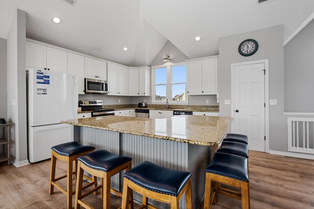 kitchen featuring stainless steel appliances, light wood-style floors, vaulted ceiling, and white cabinetry