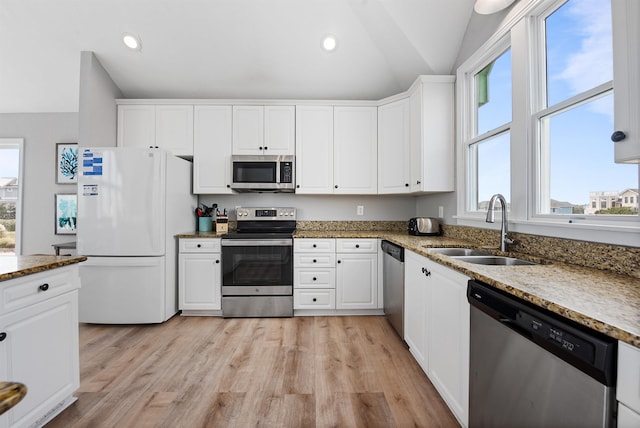 kitchen featuring light wood-type flooring, a sink, white cabinetry, stainless steel appliances, and vaulted ceiling