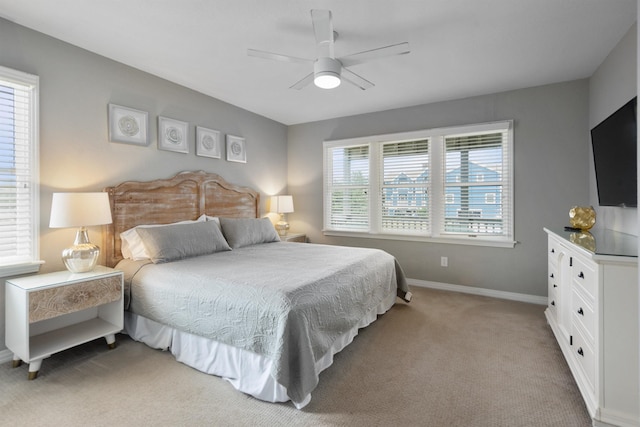 bedroom featuring baseboards, multiple windows, light colored carpet, and ceiling fan