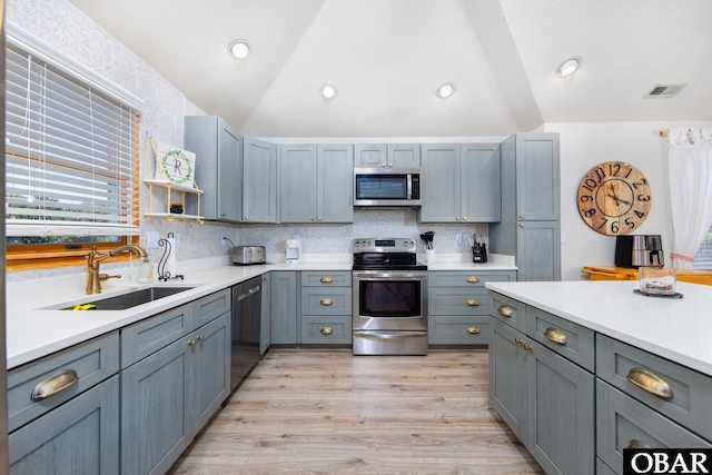 kitchen featuring appliances with stainless steel finishes, vaulted ceiling, light countertops, and a sink