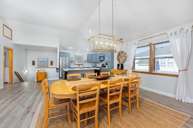 dining space with an inviting chandelier, light wood-style flooring, baseboards, and vaulted ceiling