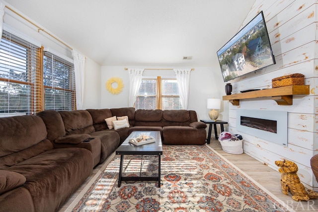 living area featuring visible vents, a glass covered fireplace, and light wood-style flooring