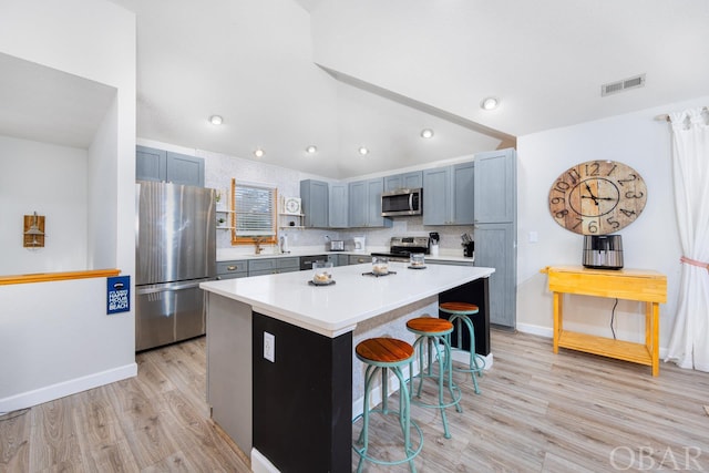 kitchen featuring stainless steel appliances, light countertops, visible vents, a kitchen island, and a kitchen breakfast bar