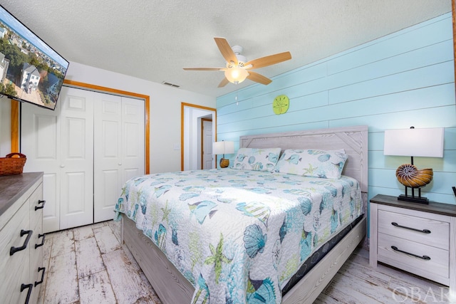 bedroom featuring a textured ceiling, ceiling fan, visible vents, a closet, and light wood finished floors