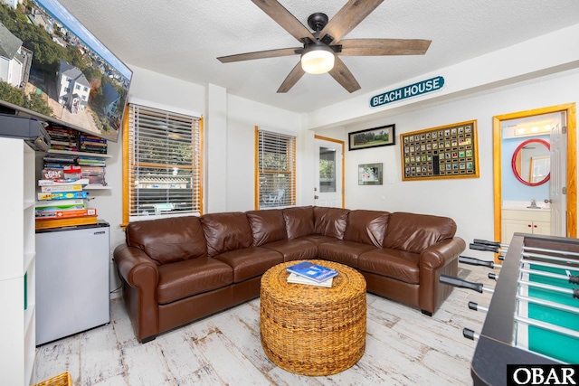 living room with light wood-type flooring, ceiling fan, and a textured ceiling