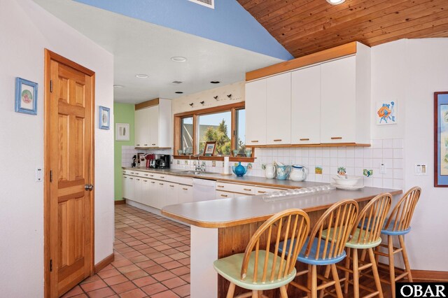 kitchen with dishwasher, light tile patterned floors, decorative backsplash, a kitchen breakfast bar, and white cabinets