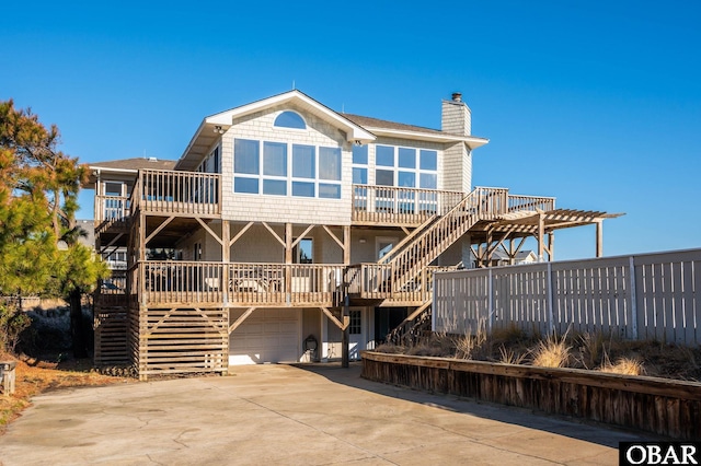 back of property featuring a wooden deck, concrete driveway, stairs, a chimney, and a garage