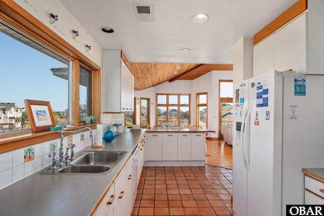 kitchen featuring visible vents, a sink, white cabinets, white refrigerator with ice dispenser, and backsplash