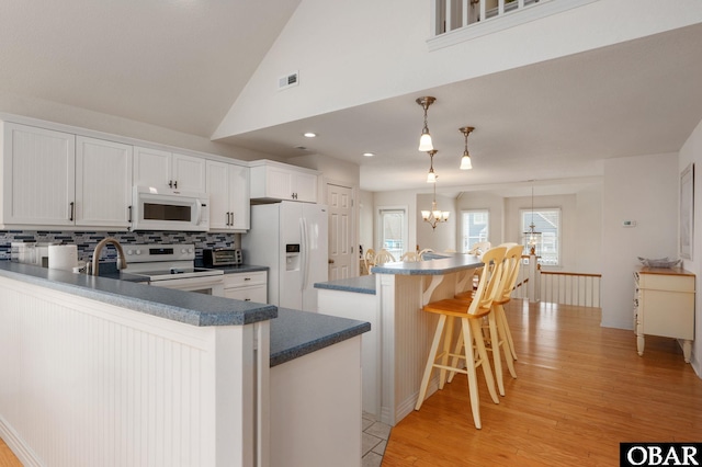 716 Moongate Ln Lot 51, Corolla, NC 27927 - kitchen with white appliances, a chandelier, decorative backsplash, light wood-style flooring, and a breakfast bar area