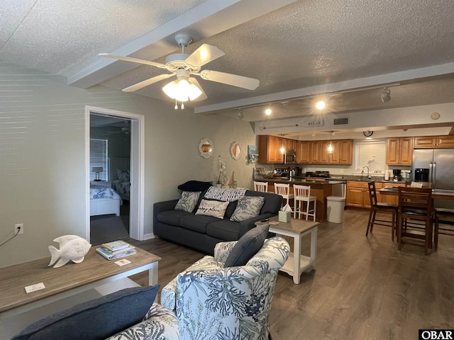 living room with a ceiling fan, a textured ceiling, dark wood-style flooring, and beamed ceiling