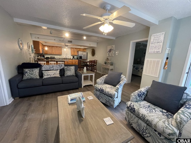 living room featuring beamed ceiling, dark wood-style flooring, a textured ceiling, and visible vents