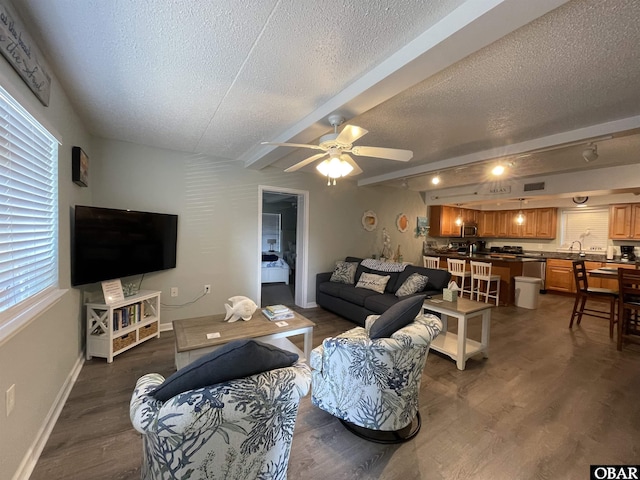 living room with beamed ceiling, a ceiling fan, a textured ceiling, and dark wood-type flooring