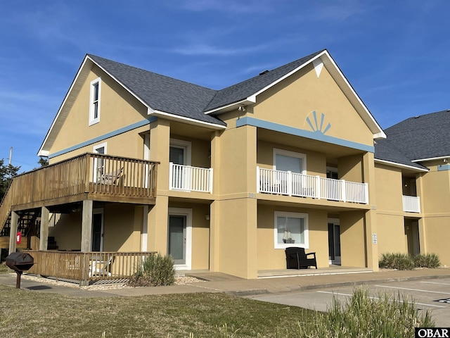 rear view of property with a shingled roof, a balcony, and stucco siding