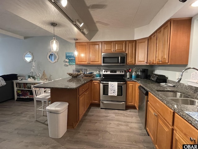 kitchen with a sink, brown cabinetry, stainless steel appliances, and a peninsula