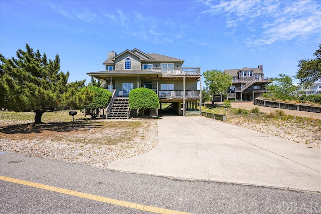 raised beach house with a carport, concrete driveway, covered porch, and stairs