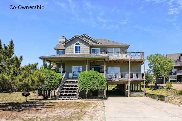 coastal home featuring covered porch, concrete driveway, stairway, a carport, and a chimney