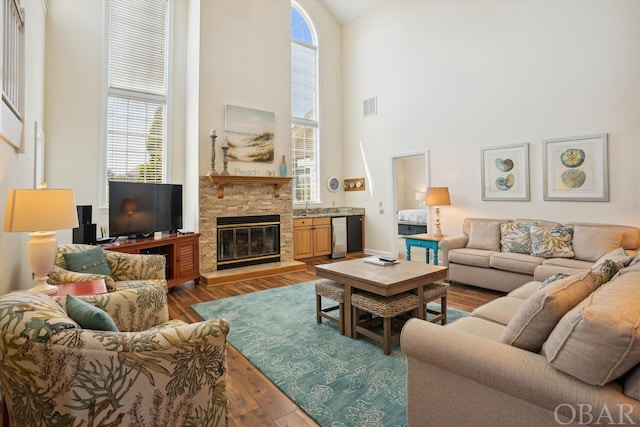 living room featuring a towering ceiling, a stone fireplace, wood finished floors, and visible vents