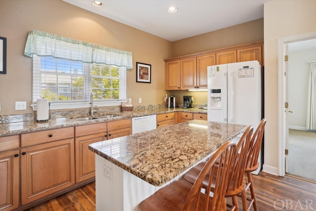 kitchen featuring white appliances, a breakfast bar, a center island, light stone countertops, and a sink