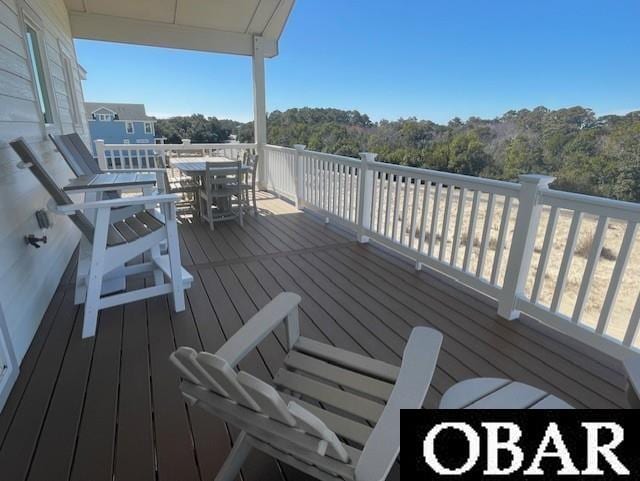 wooden terrace featuring outdoor dining space and a view of trees