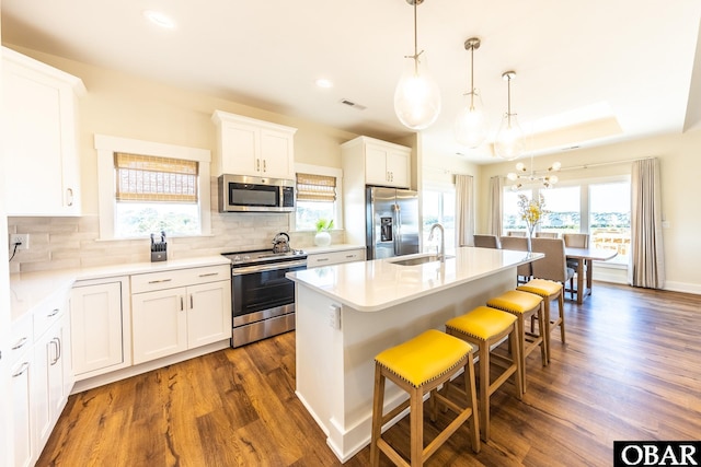 kitchen featuring a breakfast bar area, dark wood-type flooring, visible vents, appliances with stainless steel finishes, and an island with sink