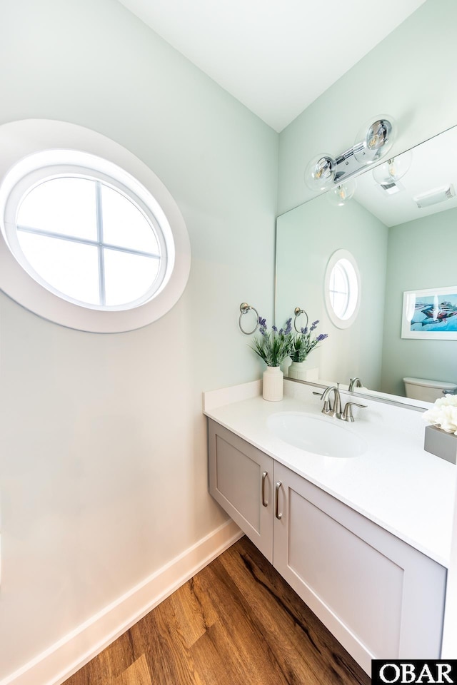 half bath featuring visible vents, baseboards, toilet, wood finished floors, and vanity