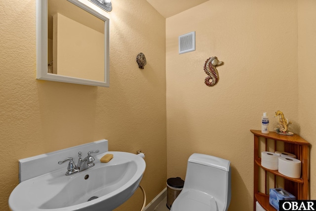 half bathroom featuring a textured wall, visible vents, a sink, and toilet