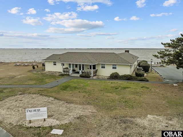 view of front of home featuring covered porch, a water view, driveway, and a front lawn