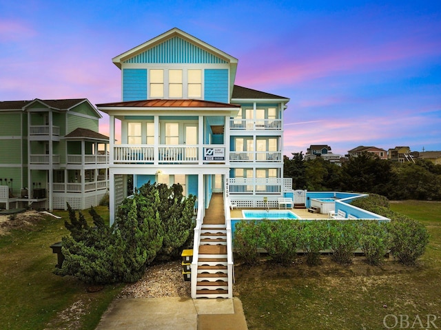 back of house featuring an outdoor pool, a balcony, stairway, a standing seam roof, and board and batten siding