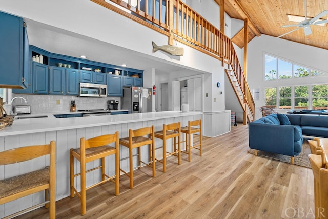 kitchen featuring blue cabinets, a peninsula, stainless steel appliances, light countertops, and a sink