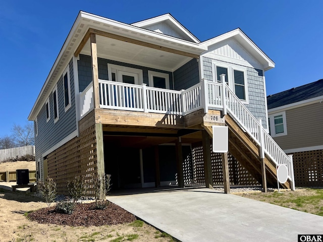 beach home featuring covered porch, concrete driveway, board and batten siding, a carport, and stairs