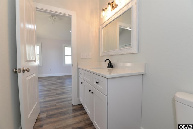 bathroom with toilet, wood finished floors, vanity, and baseboards