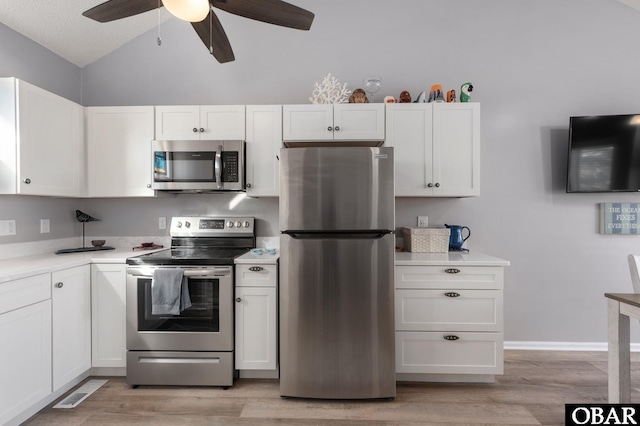 kitchen featuring stainless steel appliances, light countertops, light wood-style flooring, white cabinets, and vaulted ceiling