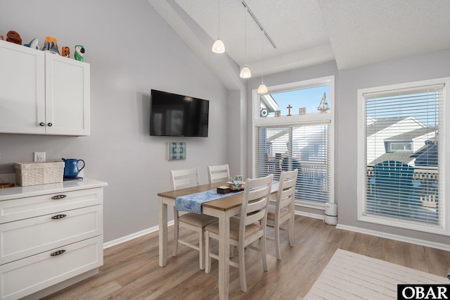 dining space featuring rail lighting, vaulted ceiling, a textured ceiling, light wood-type flooring, and baseboards