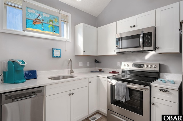 kitchen with appliances with stainless steel finishes, lofted ceiling, white cabinetry, and a sink