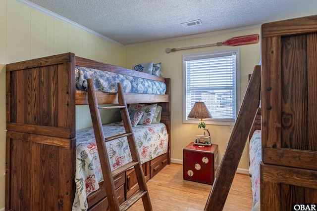 bedroom featuring visible vents, a textured ceiling, light wood-style flooring, and crown molding