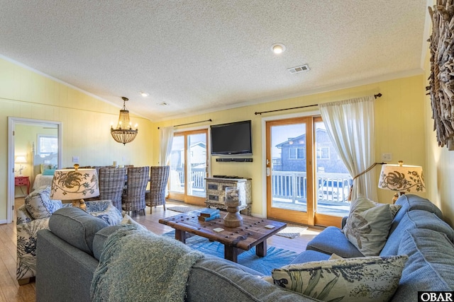 living area with a textured ceiling, wood finished floors, visible vents, vaulted ceiling, and an inviting chandelier