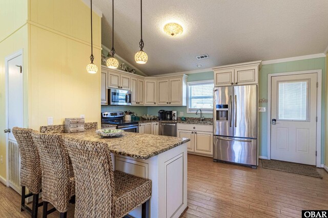 kitchen featuring cream cabinets, stainless steel appliances, a breakfast bar, a peninsula, and pendant lighting