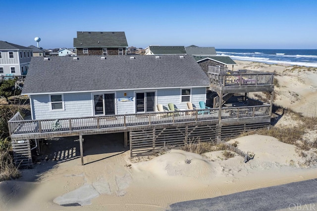 back of house with a shingled roof, a beach view, and a deck with water view