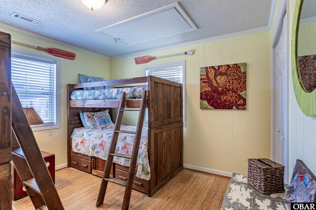 bedroom featuring light wood-style floors, visible vents, crown molding, and a textured ceiling