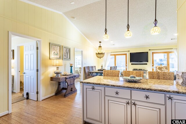 kitchen featuring vaulted ceiling, light stone counters, open floor plan, and decorative light fixtures