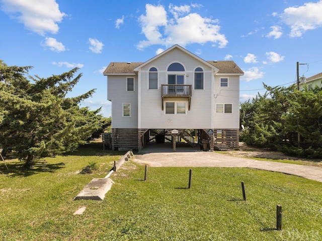 back of property featuring a yard, concrete driveway, a carport, and a balcony