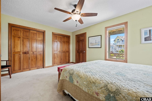 bedroom featuring carpet flooring, a textured ceiling, a ceiling fan, and two closets