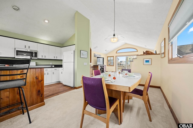 dining room with baseboards, vaulted ceiling, and light carpet