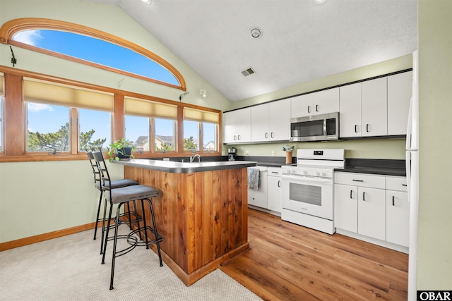 kitchen with white range with electric stovetop, dark countertops, a kitchen breakfast bar, white cabinetry, and stainless steel microwave