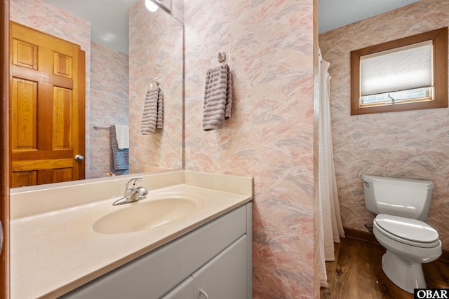 full bathroom featuring vanity, toilet, wallpapered walls, and wood finished floors