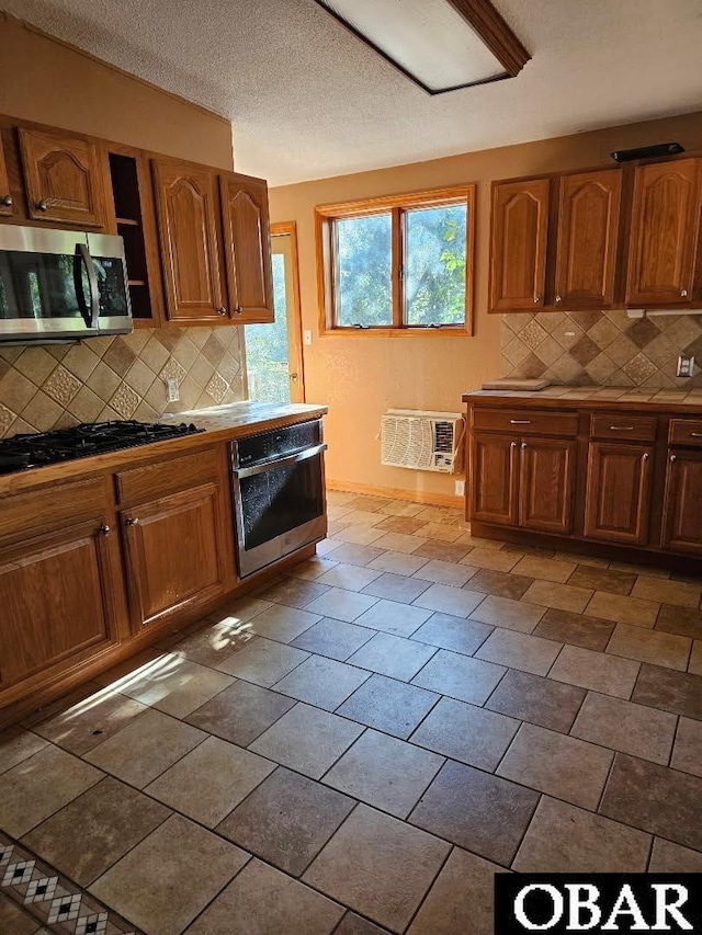 kitchen with stainless steel appliances, brown cabinetry, a wall mounted air conditioner, and backsplash