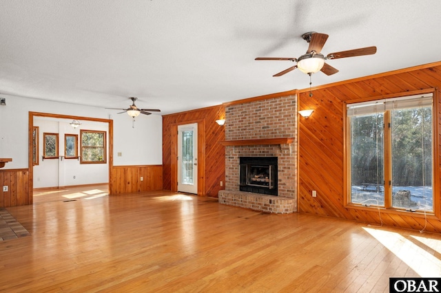 unfurnished living room with wood walls, a brick fireplace, light wood finished floors, and a textured ceiling